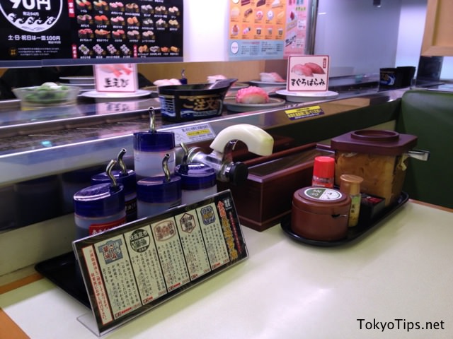 Soy sauces, green tea powder, pickled ginger slice, chopsticks, and others are set on a table. Also there is hot water tap.